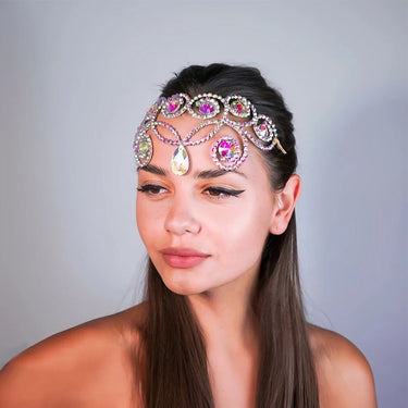 Model wearing iridescent rhinestone headpiece styled as forehead jewelry with cascading crystal detail.
